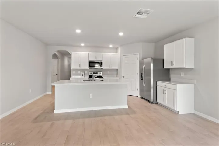 Kitchen with arched walkways, white cabinets, an island with sink, stainless steel appliances, and light wood-style flooring