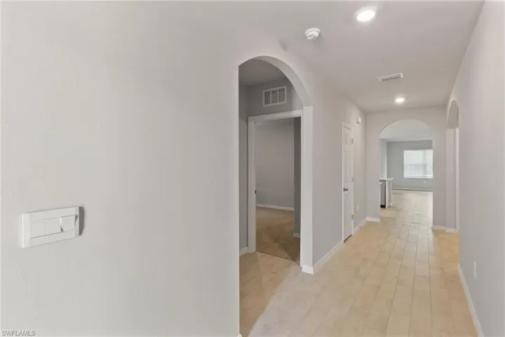 Corridor with arched walkways, light wood finished floors, and recessed lighting