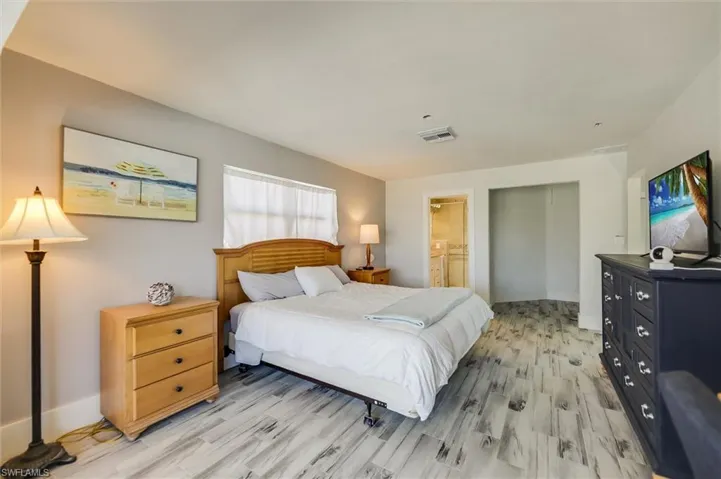 Bedroom featuring light wood finished floors, a closet, visible vents, ensuite bath, and baseboards