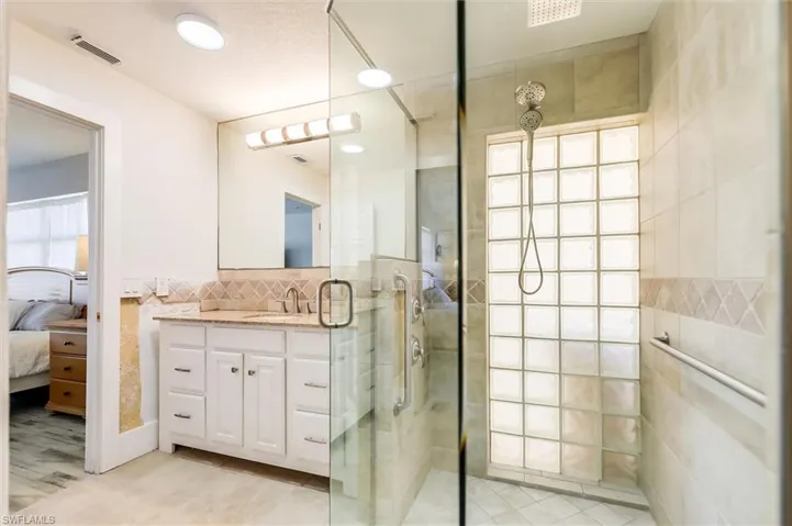Ensuite bathroom featuring visible vents, connected bathroom, vanity, a shower stall, and tile walls