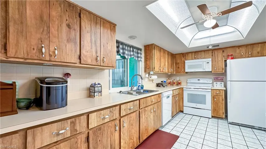 Kitchen featuring white appliances, a skylight, backsplash, sink, and ceiling fan