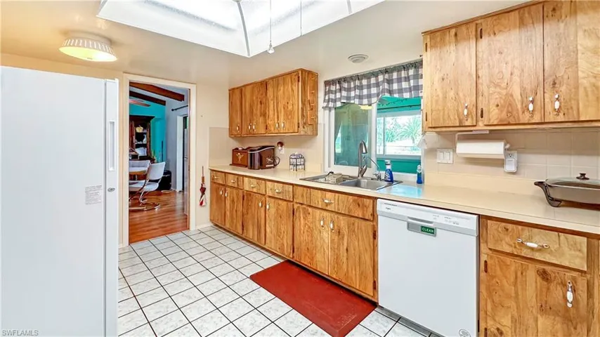 Kitchen featuring white dishwasher, tasteful backsplash, light hardwood / wood-style floors, sink, and a skylight