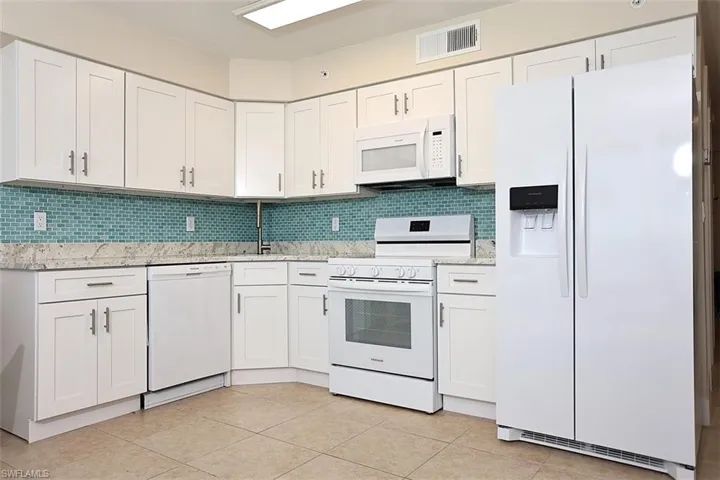 Kitchen featuring light tile patterned floors, white appliances, tasteful backsplash, and white cabinetry