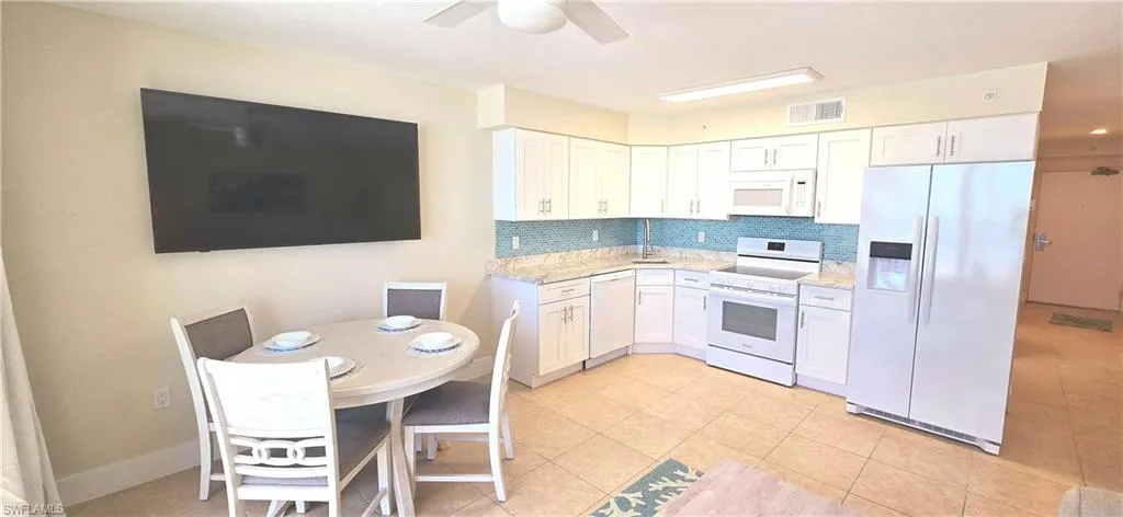 Kitchen featuring white appliances, ceiling fan, light stone countertops, tasteful backsplash, and white cabinetry