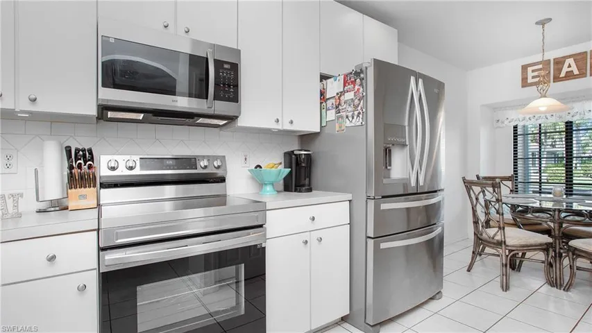 Kitchen featuring stainless steel appliances, light countertops, light tile patterned flooring, white cabinets, and backsplash
