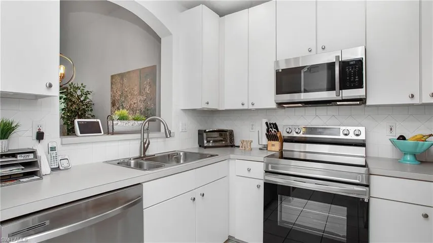 Kitchen with appliances with stainless steel finishes, light countertops, backsplash, and white cabinets
