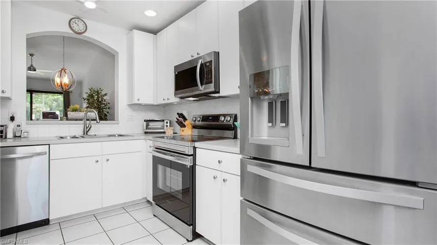 Kitchen featuring stainless steel appliances, backsplash, light countertops, arched walkways, and white cabinetry