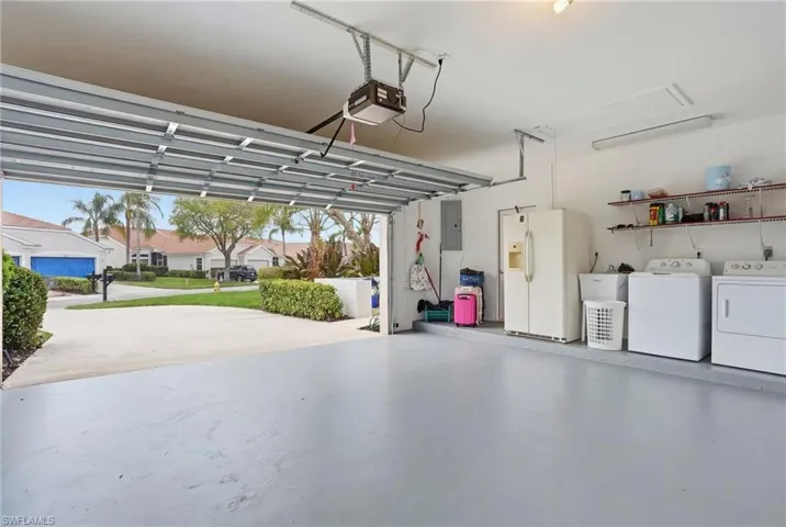 Garage featuring white refrigerator with ice dispenser, washer and dryer, electric panel, a residential view, and a garage door opener