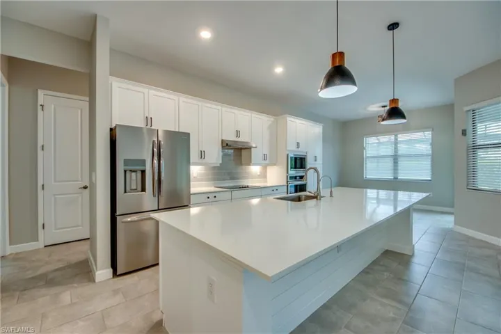 Kitchen with stainless steel appliances, white cabinets, hanging light fixtures, backsplash, and a kitchen island with sink