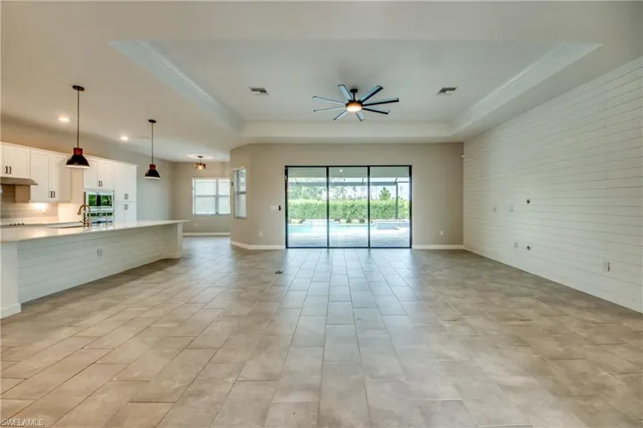 Unfurnished living room with a tray ceiling, ornamental molding, ceiling fan, wood walls, and light wood-style floors