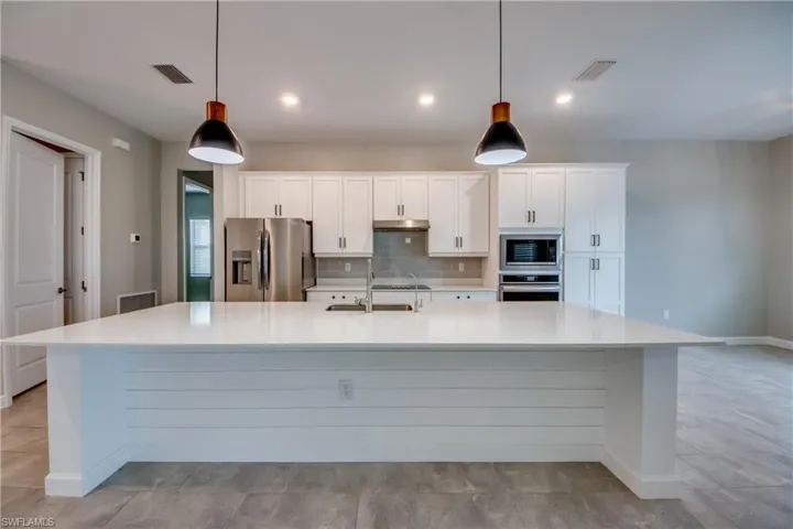 Kitchen with white cabinetry, stainless steel appliances, backsplash, a large island, and light stone counters