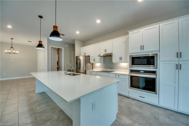 Kitchen featuring decorative backsplash, appliances with stainless steel finishes, a center island with sink, white cabinets, and pendant lighting