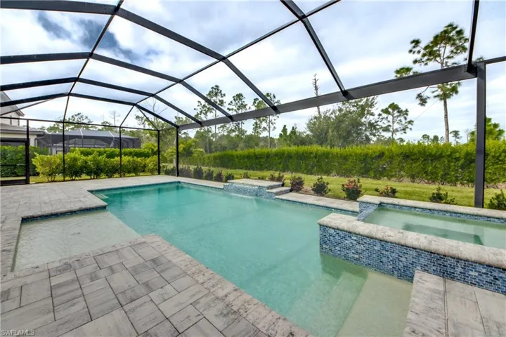 View of pool featuring glass enclosure, a sunroom, a pool with connected hot tub, and a patio