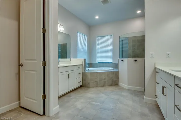 Bathroom with two vanities, a garden tub, walk in shower, light tile patterned floors, and recessed lighting
