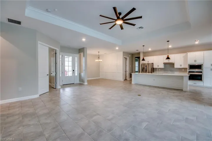 Unfurnished living room with a raised ceiling, ceiling fan, a chandelier, recessed lighting, and crown molding