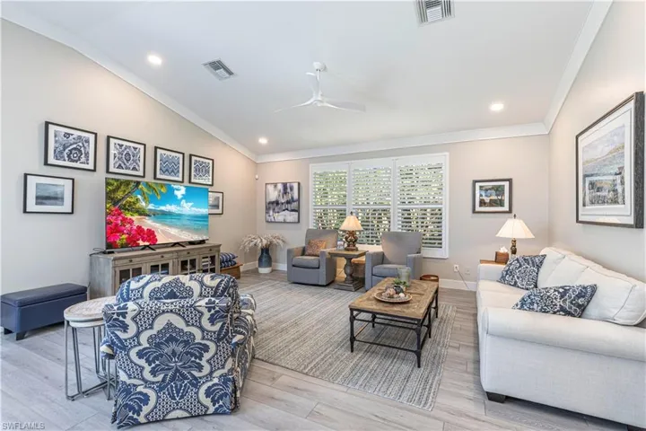Living room featuring vaulted ceiling, crown molding, wood finished floors, ceiling fan, and baseboards