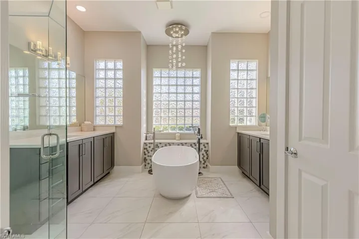 Bathroom featuring vanity, baseboards, a freestanding tub, marble look tiles, and a stall shower