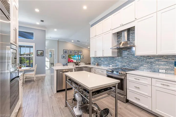 Kitchen with appliances with stainless steel finishes, wall chimney range hood, ornamental molding, a peninsula, and decorative backsplash