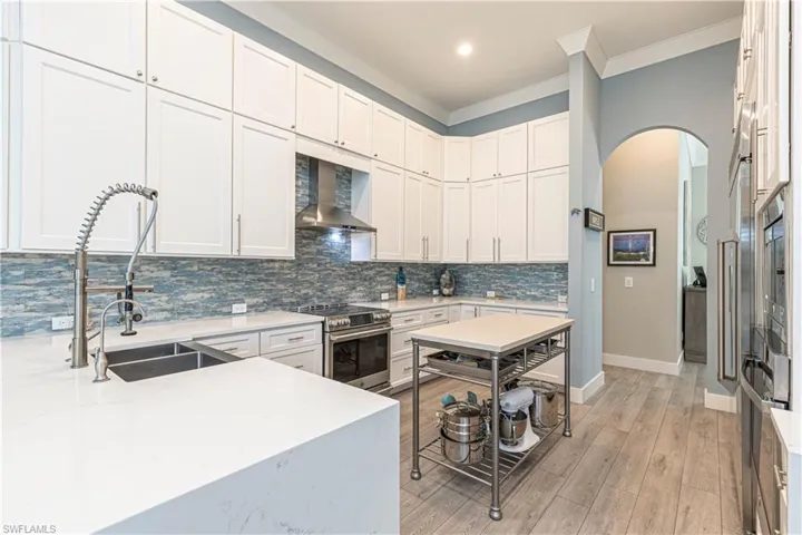 Kitchen featuring stainless steel electric range, wall chimney exhaust hood, a sink, arched walkways, and ornamental molding