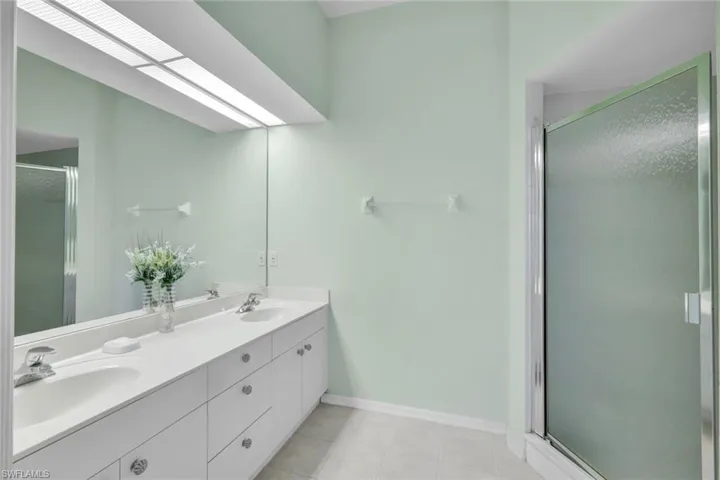Full bathroom featuring a shower stall, double vanity, and light tile patterned floors