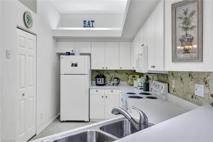 Kitchen with white appliances, light countertops, tasteful backsplash, white cabinetry, and light tile patterned floors
