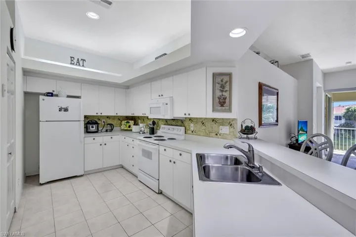Kitchen featuring white appliances, light countertops, white cabinets, decorative backsplash, and light tile patterned floors