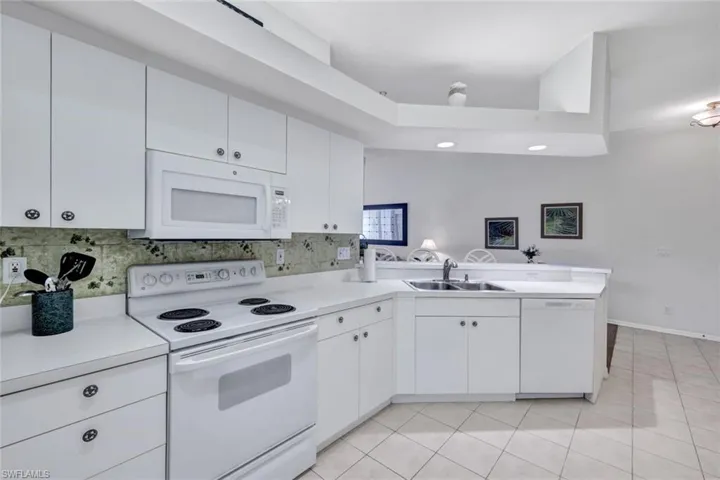 Kitchen with white appliances, a peninsula, white cabinetry, light countertops, and light tile patterned floors