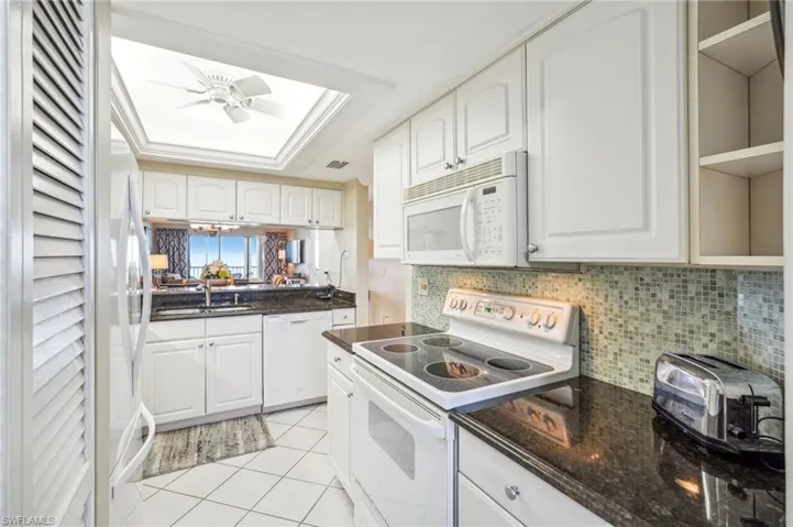 Kitchen featuring white cabinetry, light tile patterned floors, and white appliances