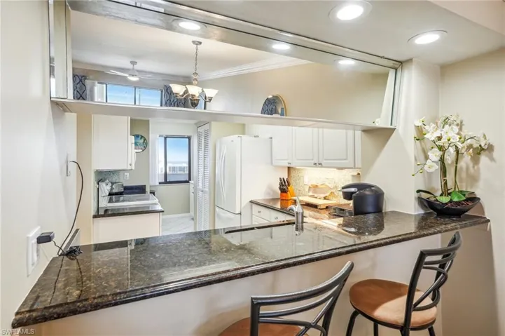 Kitchen with dark stone counters, white cabinets, hanging light fixtures, and white refrigerator