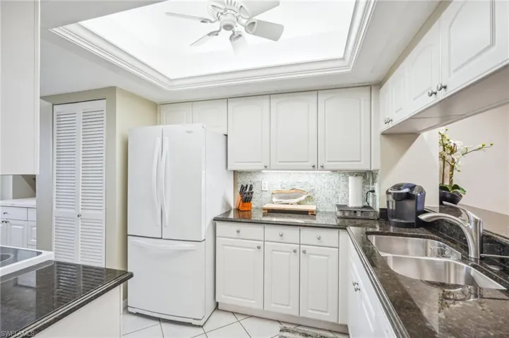 Kitchen featuring white cabinets, white fridge, sink, and a tray ceiling
