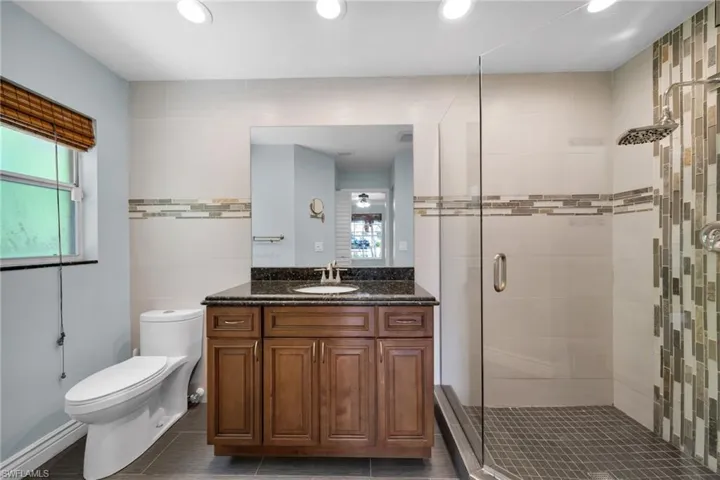 Full bath featuring vanity, a stall shower, tile walls, and recessed lighting