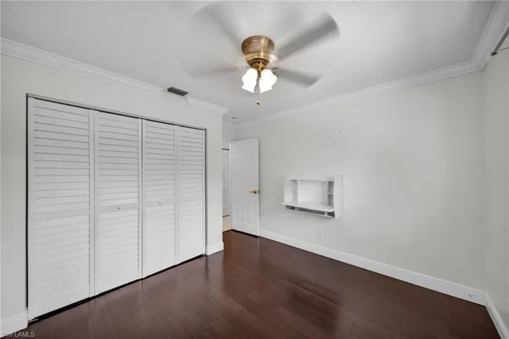 Unfurnished bedroom with ornamental molding, dark wood-style flooring, a closet, and a ceiling fan