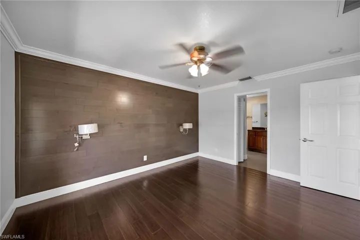 Unfurnished bedroom with ornamental molding, wood walls, an accent wall, ensuite bath, and dark wood-type flooring