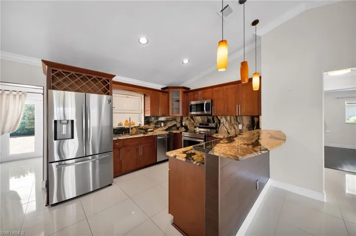 Kitchen with crown molding, dark stone countertops, stainless steel appliances, vaulted ceiling, and healthy amount of natural light