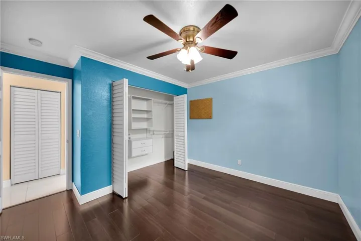Unfurnished bedroom with crown molding, dark wood-style floors, a closet, and a ceiling fan