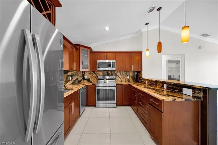 Kitchen featuring stainless steel appliances, light stone countertops, backsplash, decorative light fixtures, and glass insert cabinets