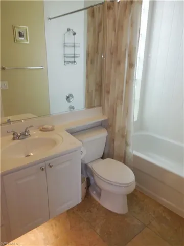 Full bathroom featuring shower / tub combo with curtain, vanity, tile patterned floors, and toilet