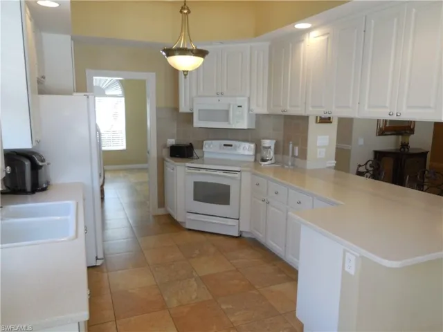 Kitchen featuring kitchen peninsula, hanging light fixtures, white appliances, and tasteful backsplash