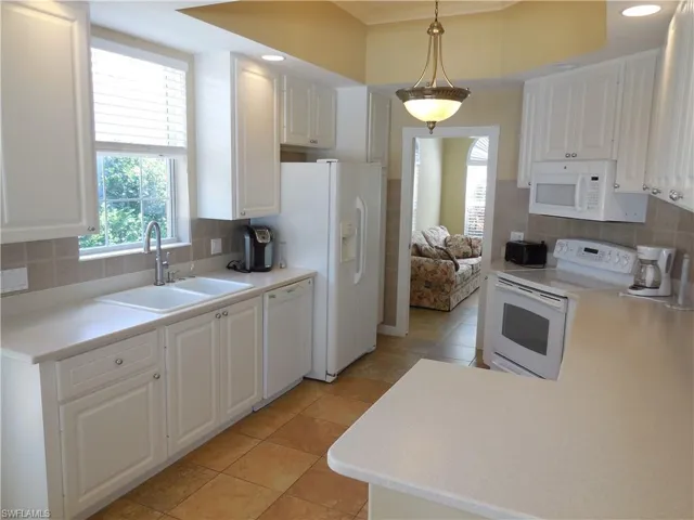 Kitchen featuring white appliances, sink, decorative light fixtures, backsplash, and white cabinetry
