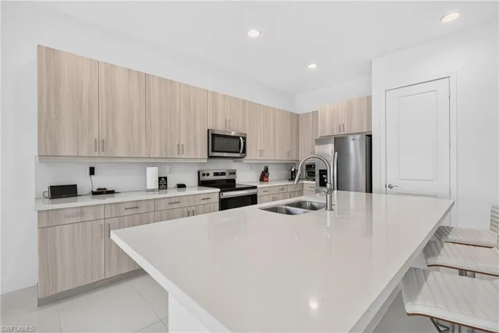 Spacious kitchen featuring a large island with an undermount double sink, extensive light wood-finish cabinetry, stainless steel appliances, and recessed lighting