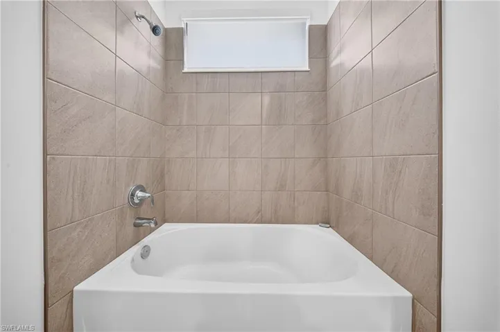 Bathtub with tile surround, chrome fixtures, and an integrated window