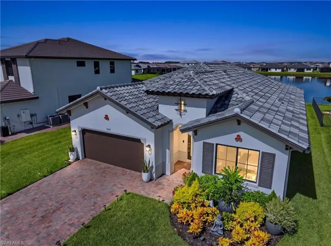 Stucco exterior with a tile roof, decorative shutters, paver driveway, and landscaped garden