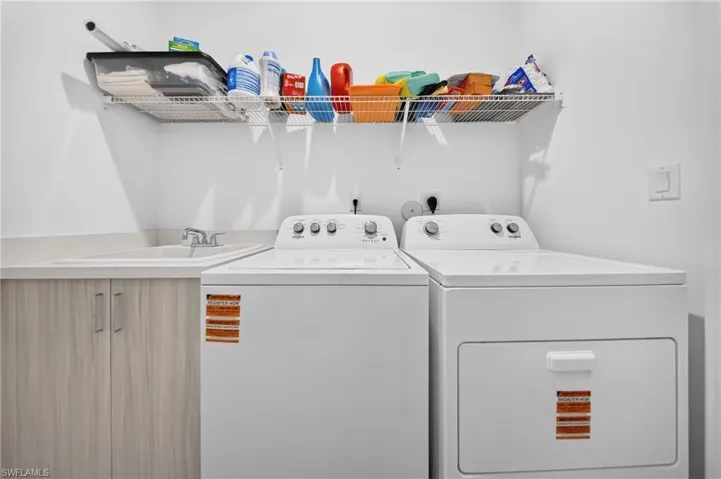 Utility room featuring a built-in sink, base cabinetry with wood-finish doors, and an overhead wire shelf
