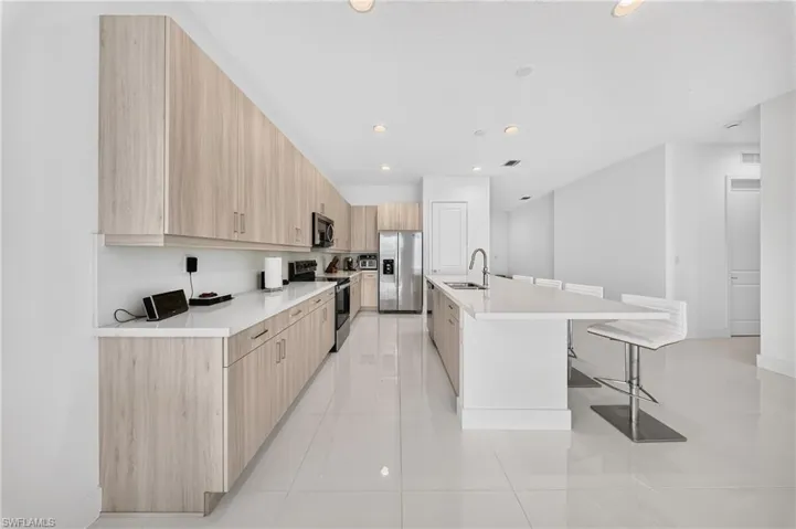 Kitchen featuring wood-finish cabinetry, white countertops, stainless steel appliances, a large center island with seating, and tiled flooring