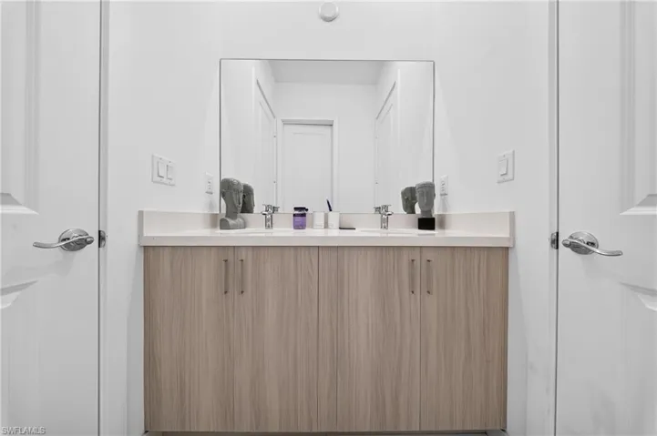 Double vanity with a light wood-finish cabinet, dual undermount sinks, single-handle chrome faucets, and a large wall-mounted mirror
