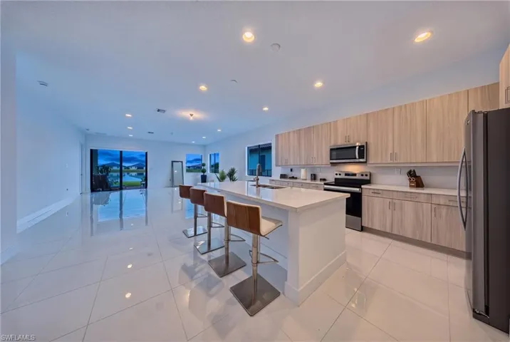 Open-concept living space with polished tile flooring, a large kitchen island with seating, extensive cabinetry with light wood-finish, and stainless steel appliances
