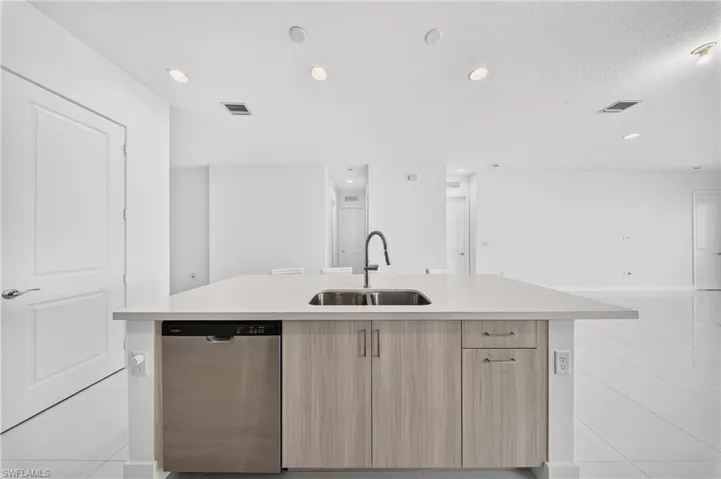 Kitchen island with a stainless steel sink, contemporary faucet, light wood-finish cabinetry, and a stainless steel dishwasher