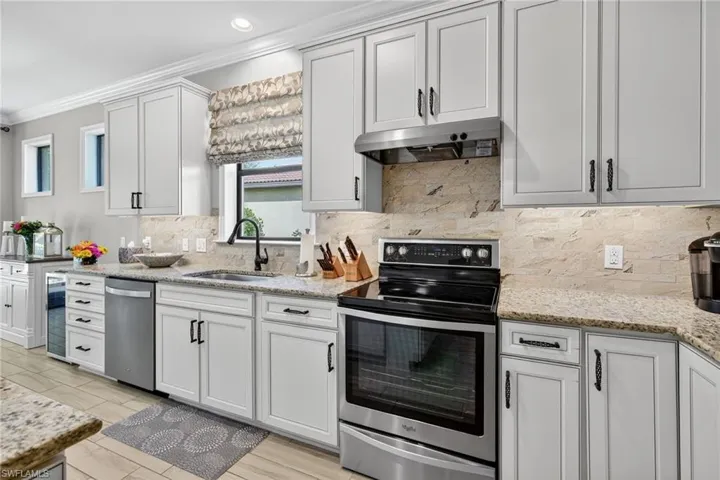 Kitchen featuring stainless steel appliances, light stone counters, backsplash, crown molding, and under cabinet range hood