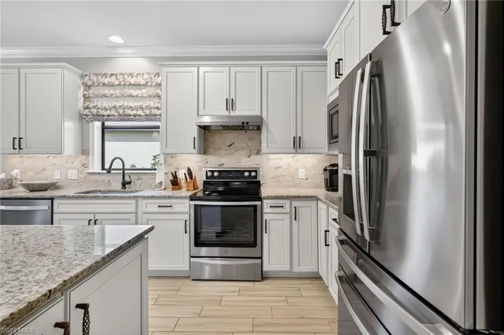 Kitchen featuring appliances with stainless steel finishes, ornamental molding, light stone countertops, tasteful backsplash, and recessed lighting