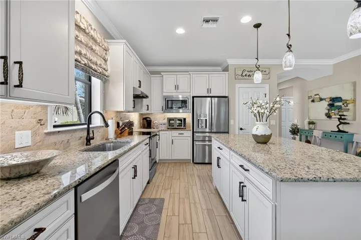 Kitchen with ornamental molding, white cabinets, stainless steel appliances, pendant lighting, and light stone countertops